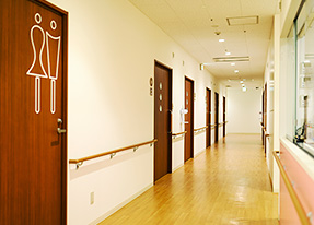 写真：梶山医院内の様子。木目調の廊下、白い壁と天井。各部屋のドアは濃い茶色の木目になっている。