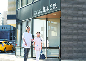 写真：梶山医院入口の前を歩いている、梶山医院長とカバンを持った女性スタッフ。